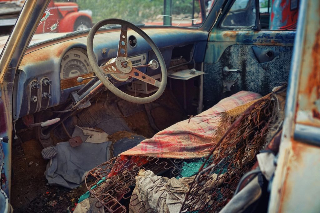 Explore the decaying, rusty interior of an abandoned car in a junkyard, full of vintage charm.